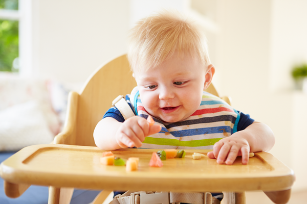 A baby sitting in a high chair eating fruit