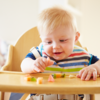 A baby sitting in a high chair eating fruit: A baby sitting in a high chair eating fruit