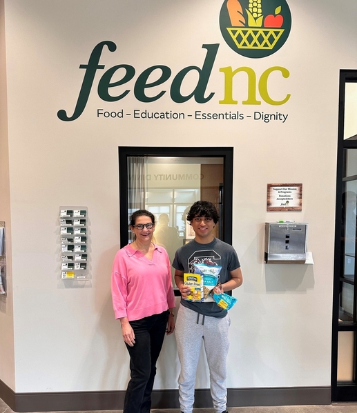 A woman and a man stand below a sign that says FeedNC holding an allergy-friendly food donation from FOODiversity