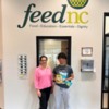 A woman and a man stand below a sign that says FeedNC holding an allergy-friendly food donation from FOODiversity: A woman and a man stand below a sign that says FeedNC holding an allergy-friendly food donation from FOODiversity