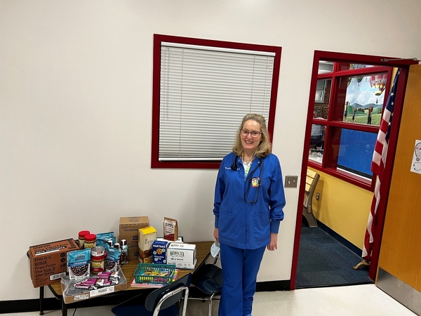 A woman in blue scrubs standing next to a table of allergy-friendly food donated from FOODiversity
