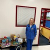 A woman in blue scrubs standing next to a table of allergy-friendly food donated from FOODiversity: A woman in blue scrubs standing next to a table of allergy-friendly food donated from FOODiversity