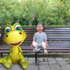 Boy sitting on a park bench next to a cartoon dinosaur: Boy sitting on a park bench next to a cartoon dinosaur